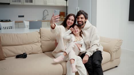 Una-Familia-Feliz-Y-Sonriente-Está-Haciendo-Una-Selfie-O-Una-Videollamada-Con-Un-Teléfono-Inteligente-En-Un-Sofá-De-Una-Sala-De-Estar