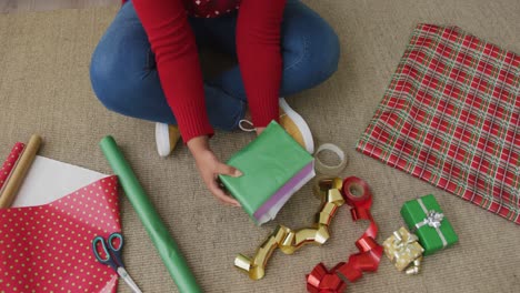 mujer afroamericana de talla grande con sombrero de papá noel, empacando regalos en la sala de estar en navidad