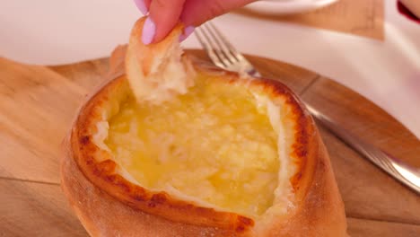 closeup hand takes bread piece puts into khachapuri filling