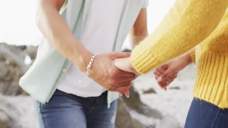 Mid-section-of-african-american-couple-holding-hands-on-the-rocks-near-the-sea