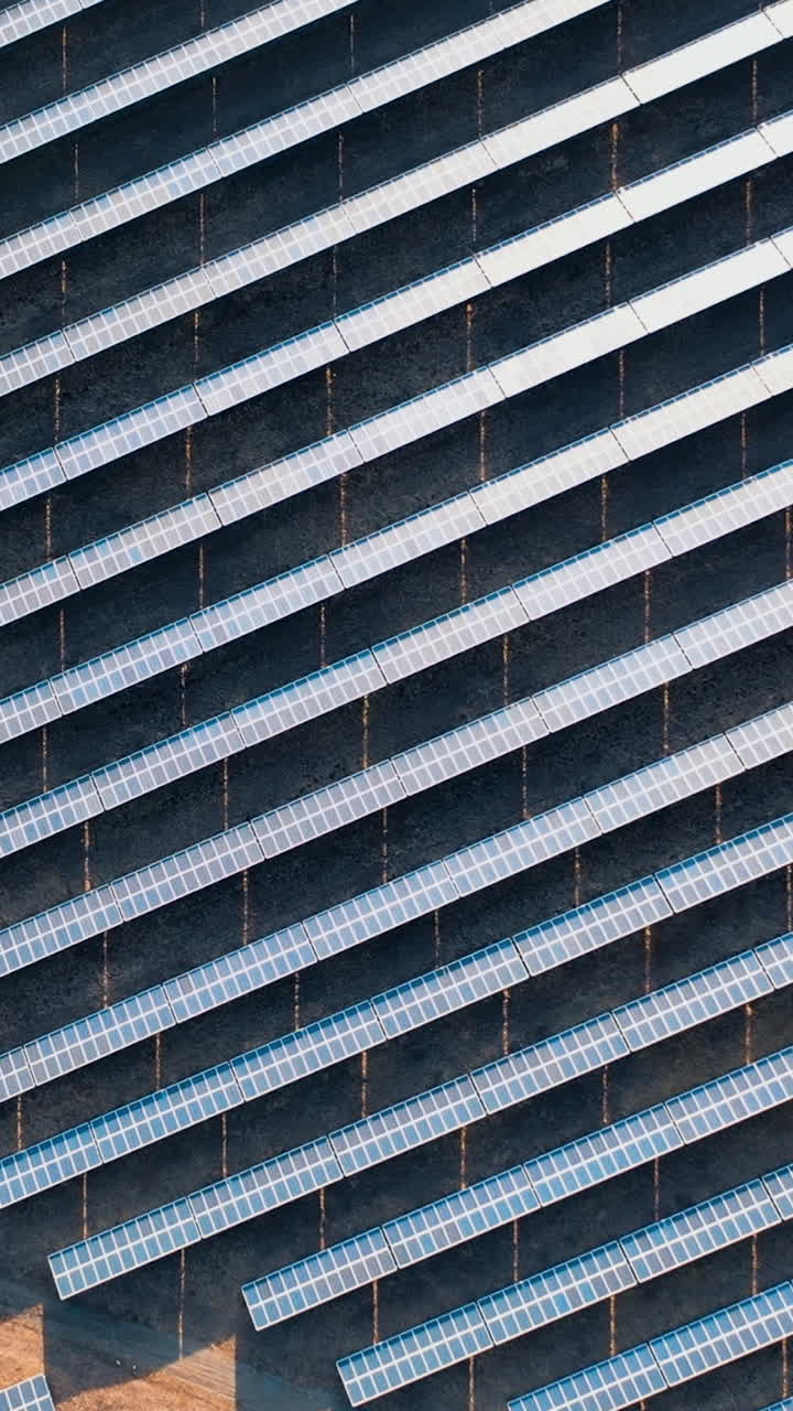 Sunset aerial view of solar panels stand in a row in the dark fields. Green energy landscape electrical power. Camera rotate. Vertical video