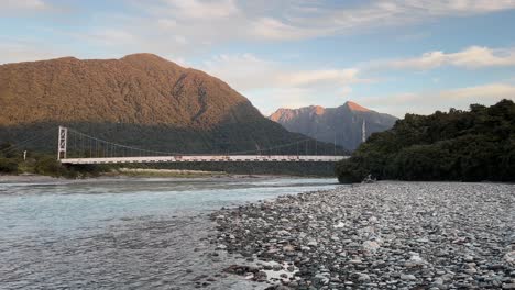 old karangarua steel bridge with towering mountains bathed in orange sunset light in background