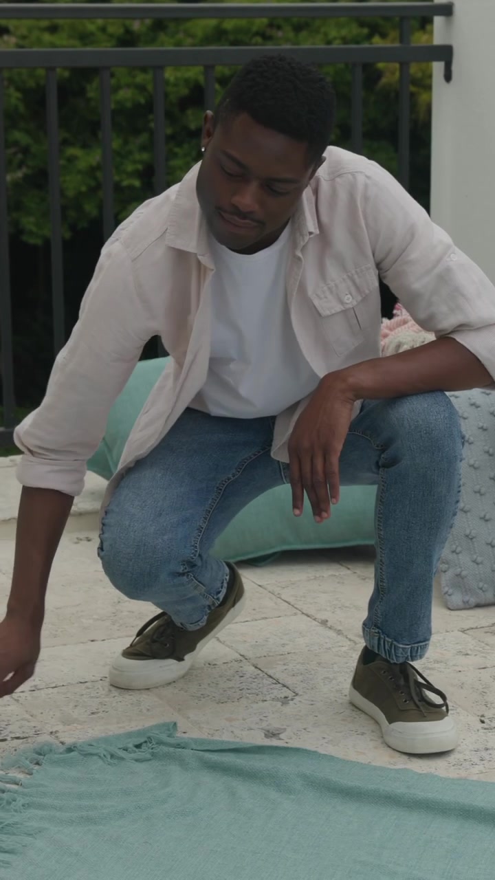 Vertical video: Adult African American man holding throw, preparing patio picnic, copy space