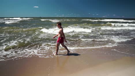 Young-man-in-red-shorts-walks-in-a-beach-by-the-sea