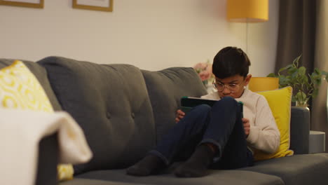 young boy sitting on sofa at home playing games or streaming onto digital tablet 5