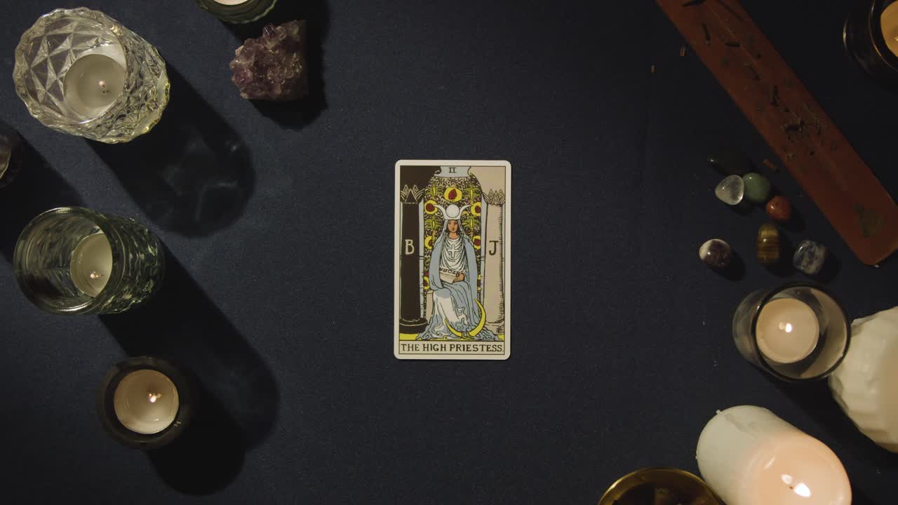 toma aérea de una persona que da una lectura de cartas del tarot colocando la carta de la alta sacerdotisa en la mesa
