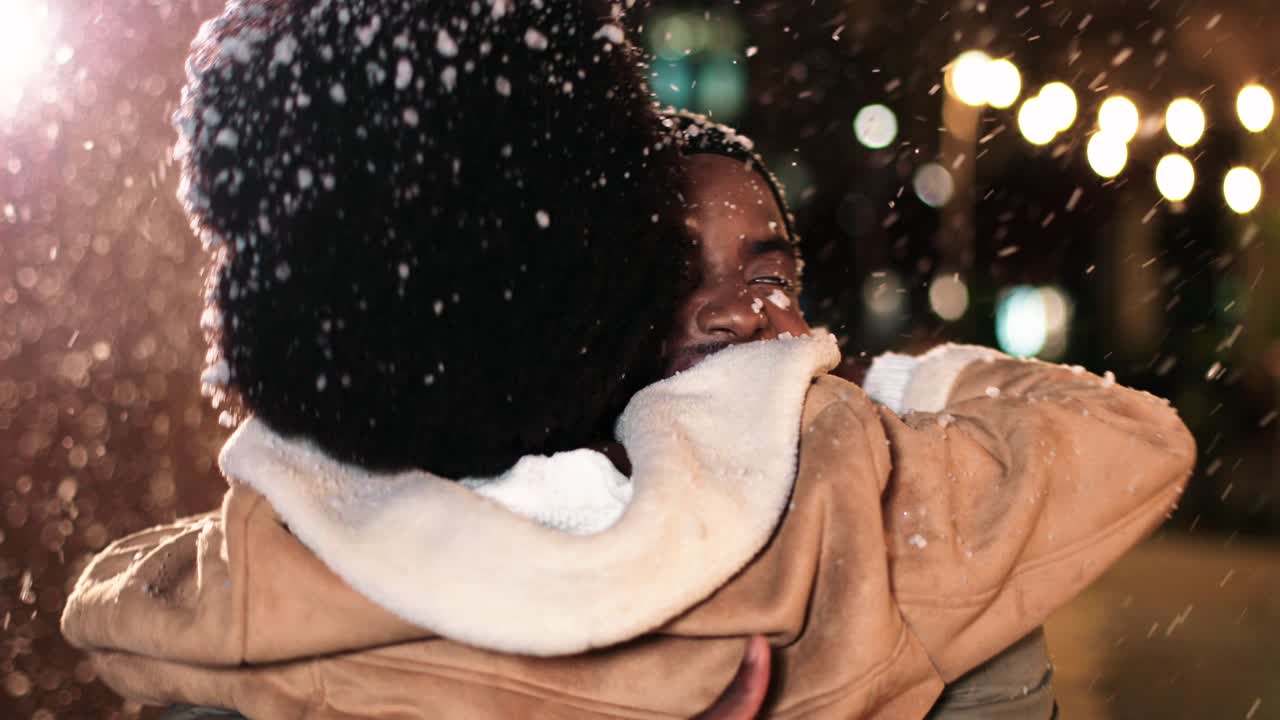 Close-up view of joyful African American couple hugging and smiling while it¬¥s snowing on the street in Christmas