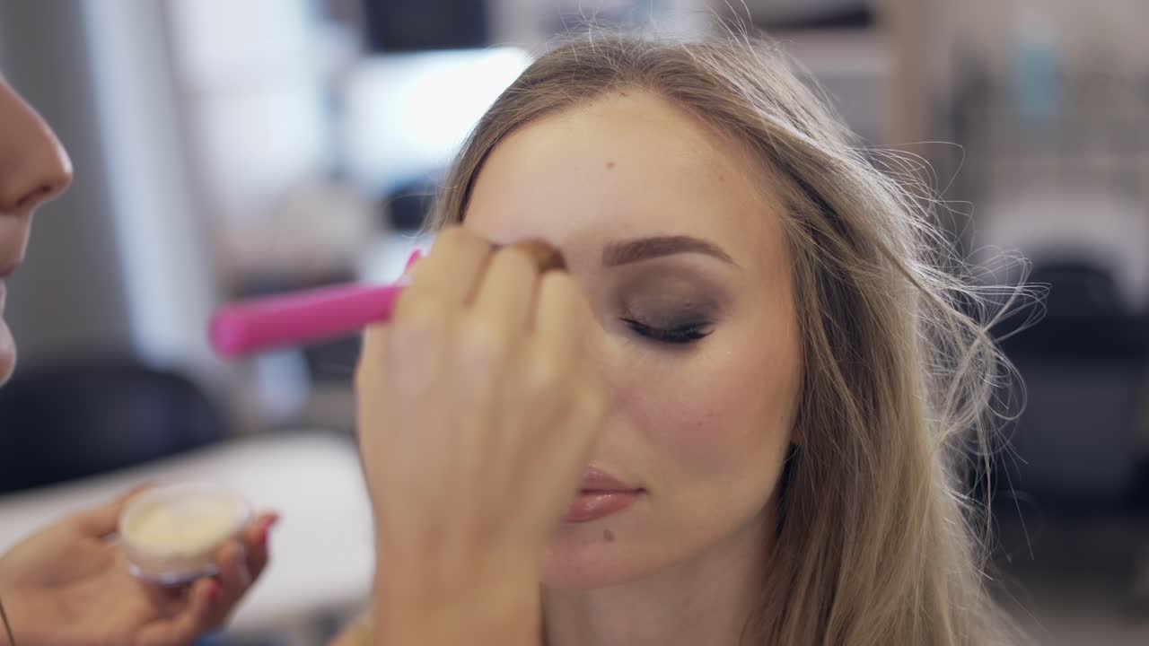 el artista de maquillaje aplica el polvo de acabado con pincel en el estudio brillante