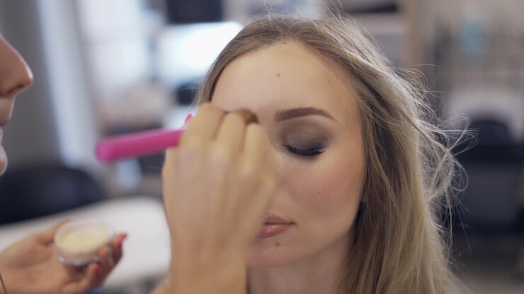 The make-up artist applies the finish powder with brush at bright studio