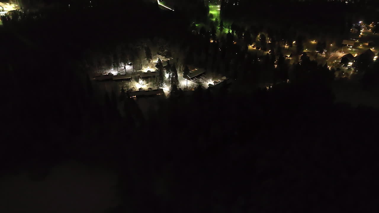 Aerial view rotating toward a illuminated cabin village, winter night in Finland
