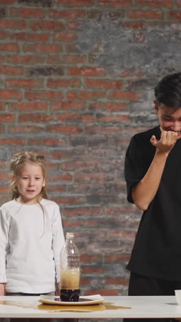 emotional little preschooler girl points to spilled soda drink on table to asian man tutor after scientific experiment in home lab slow motion