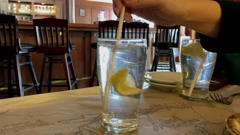 una señora caucasion, usando una pajita de papel blanco, está revolviendo un limón en un vaso de agua helada