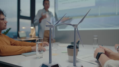 wind turbine models on meeting table in the office of eco-friendly company, colleagues discussing presentation in the background. close-up shot