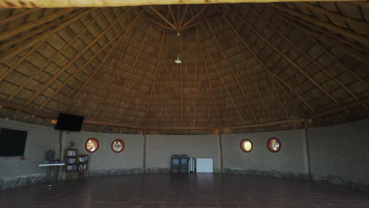 Superadobe house interior with rustic thatched roof and circular windows. Vertical view, boom job down reveals recreational room