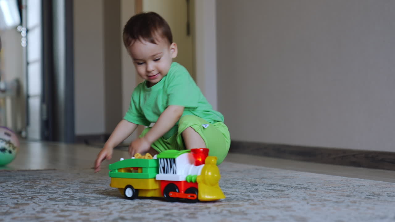 Healthy Caucasian baby boy playing with a train. Toy vehicle goes away and kid cheerfully follows it.