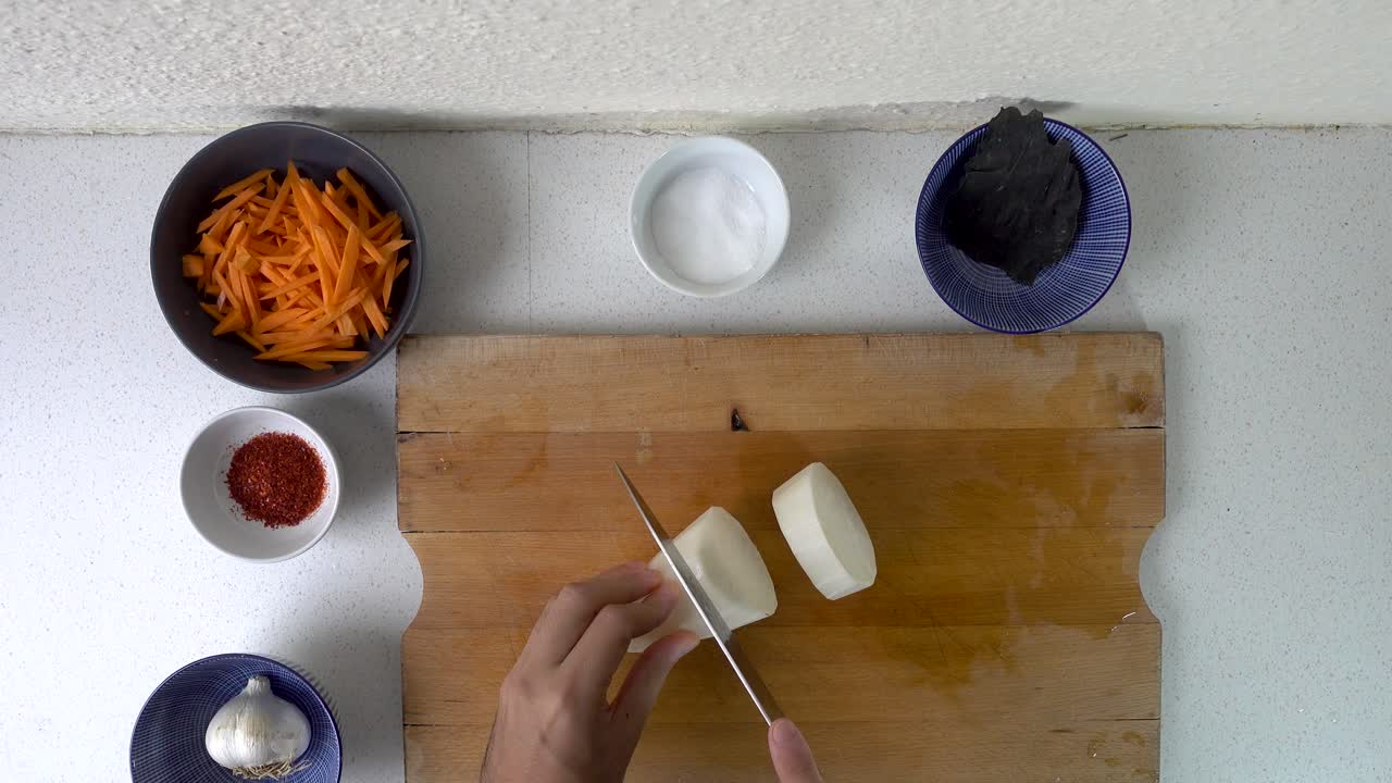 manos preparando rábano daikon en la tabla de cortar, mirando hacia abajo