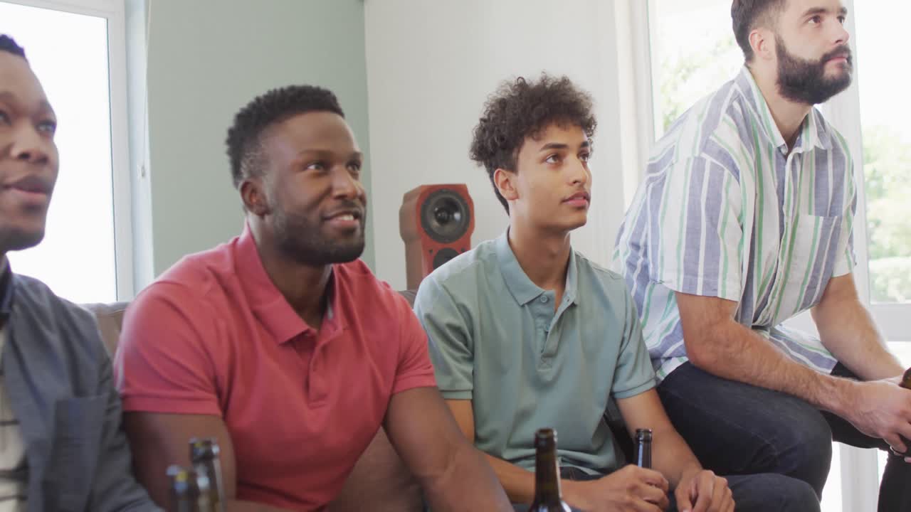 felices amigos varones diversos viendo televisión y bebiendo cerveza en la sala de estar