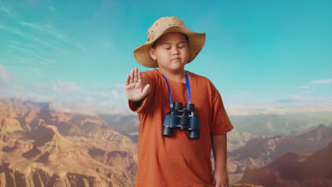 asian boy with a hat and binoculars shaking head waving hand showing no gesture avoid offer while traveling at the top of mountain. boy researcher, travel tourism adventure concept