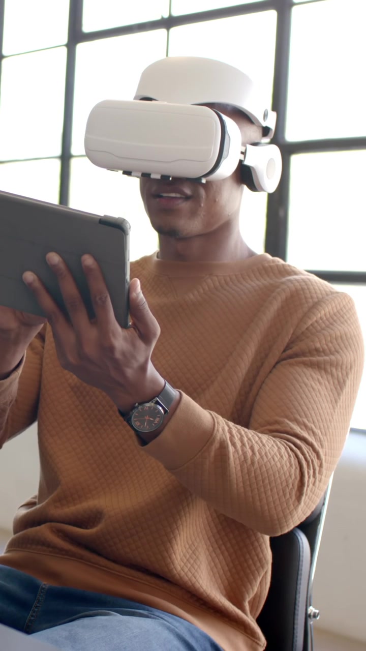 African American man wearing white VR headset and camel sweater at office holding tablet
