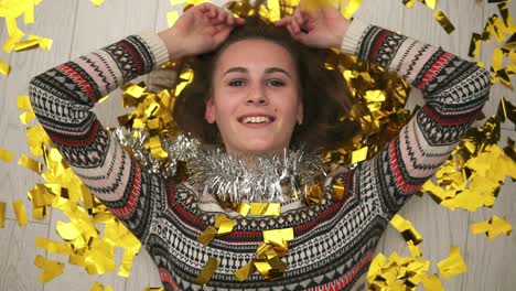 Happy-smiling-girl-lying-on-the-floor,-the-golden-confetti-falling-on-her.-After-party-time.-Close-Up-view.-Slow-motion-shot