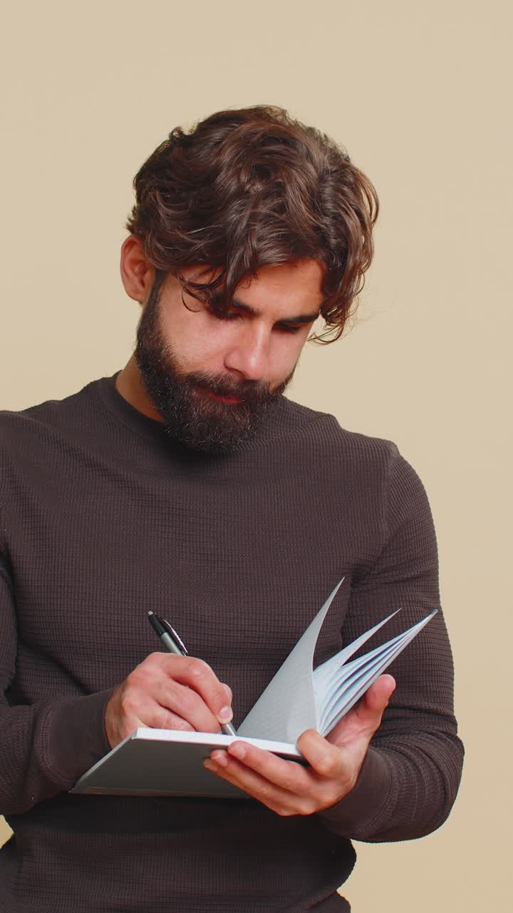 Thoughtful businessman making notes writing down thoughts with pen into diary on beige background