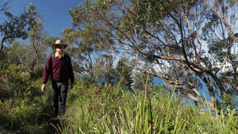 Un-Hombre-Mayor-Con-Sombrero-En-Una-Caminata-Por-El-Monte-Se-Detiene-Para-Disfrutar-De-La-Vista-Del-Océano-Desde-El-Camino-De-La-Cima-Del-Acantilado