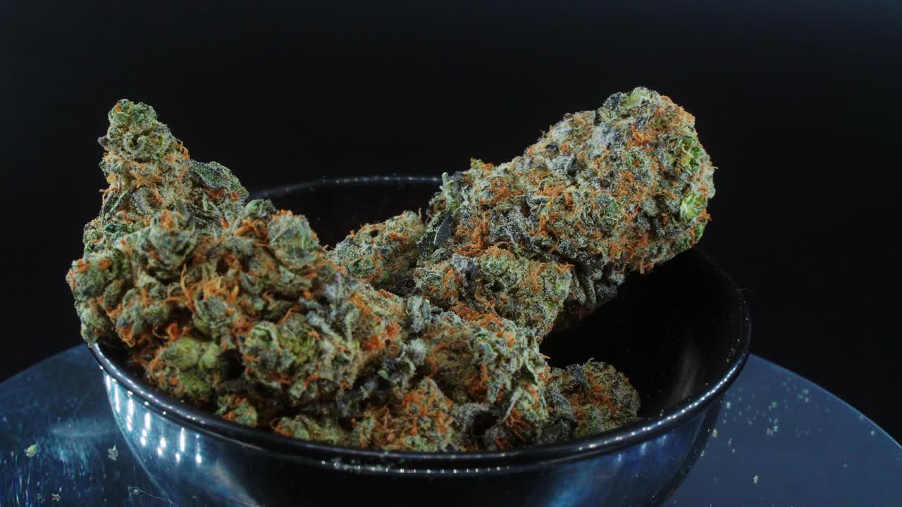 Purple Green Dried Marijuana Buds Close Up concept Shot, pile of dried marijuana plants, orange trichomes strains, in small black shiny bawl, on a rotating stand, studio lights, slow motion, 4K video