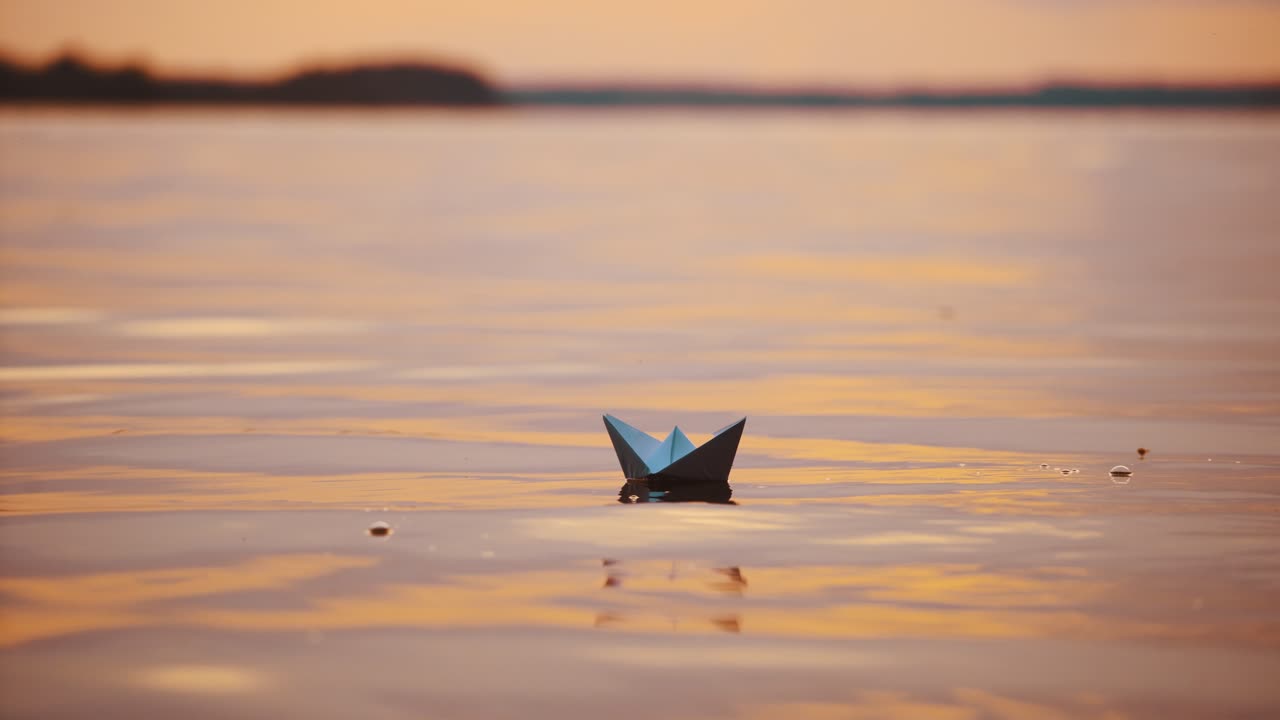 Paper ships on water surface at sunset. One origami boat floating in the river and another one joins to it.