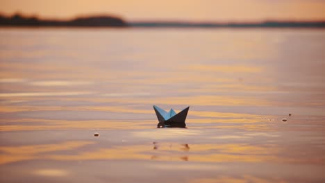 paper ships on water surface at sunset. one origami boat floating in the river and another one joins to it.