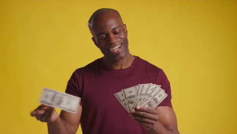 studio shot of excited mature man celebrating winning cash prize kissing counting and throwing handful of 100 dollar bills in the air