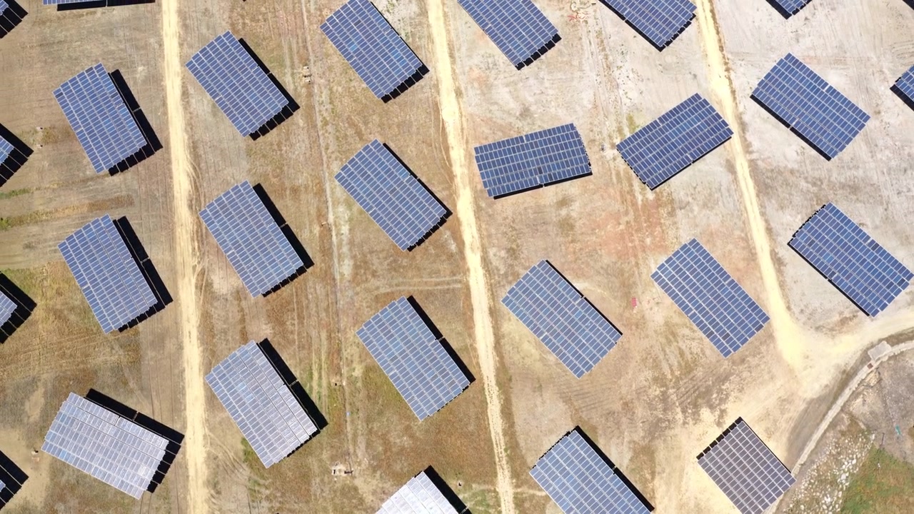 Filmato cinematografico con drone che sorvola un grande impianto fotovoltaico con pannelli che generano elettricità pulita e rinnovabile. Infrastruttura energetica sostenibile a supporto della transizione energetica globale.