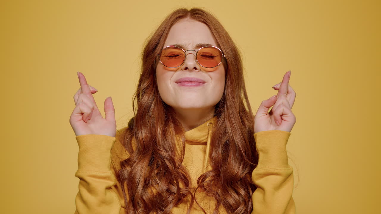Ragazza dai capelli rossi che incrocia le dita come portafortuna in studio. Donna carina che spera al chiuso