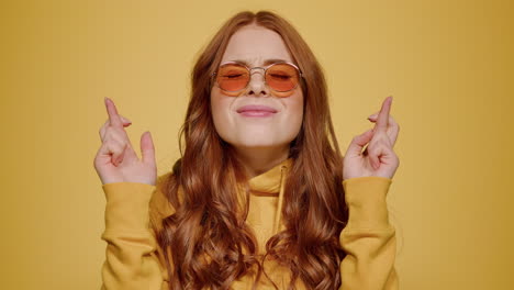 Redhead-girl-crossing-fingers-for-luck-in-studio.-Cute-woman-hoping-indoors