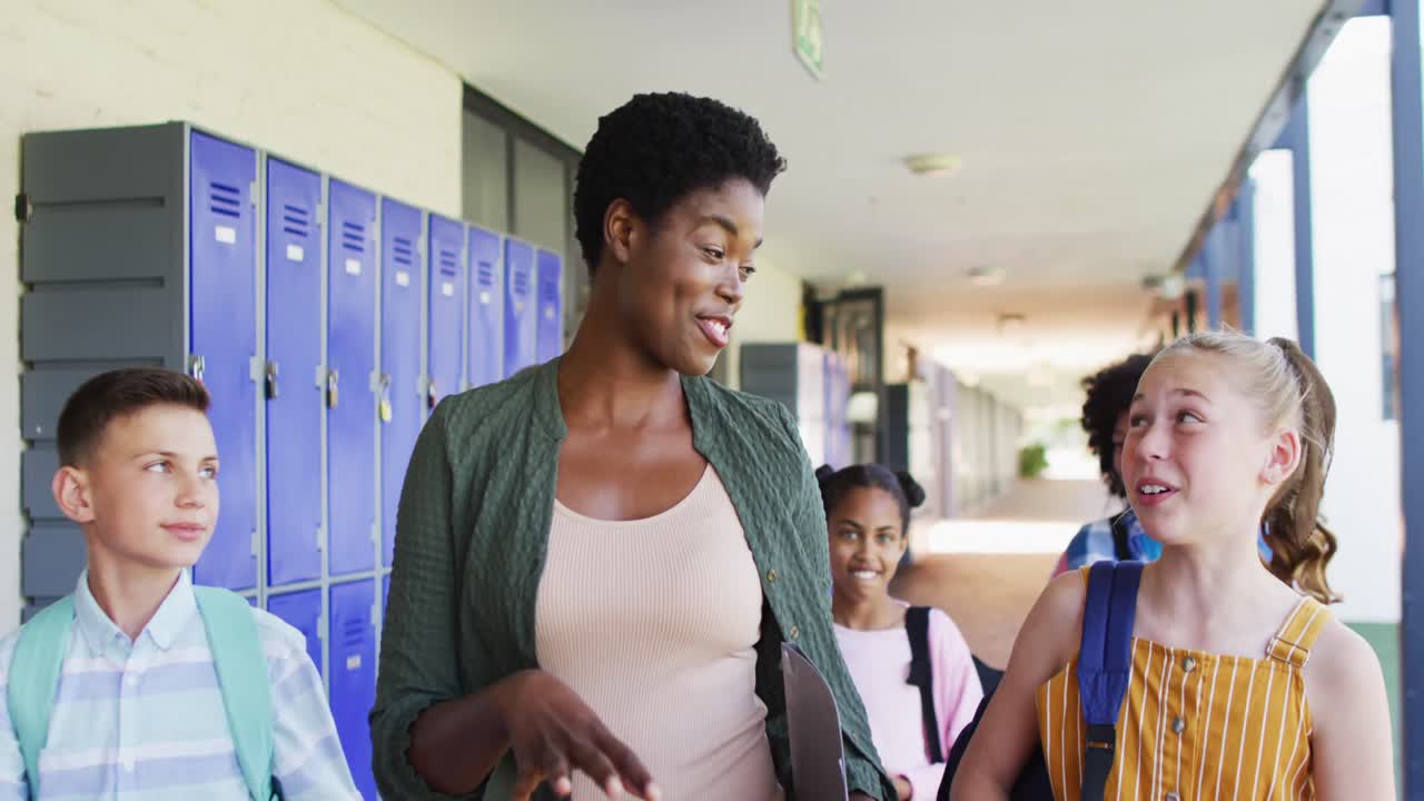 Diverse female teacher and happy schoolchildren walking in school