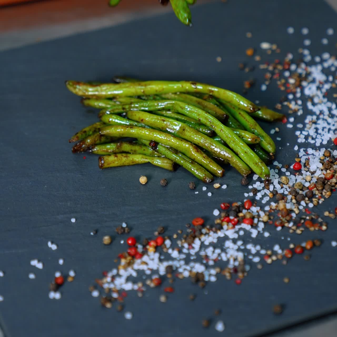 Fried green beans are put on the black charcuterie board. The plate is decorated with salt and pepper. Close up. Vertical view