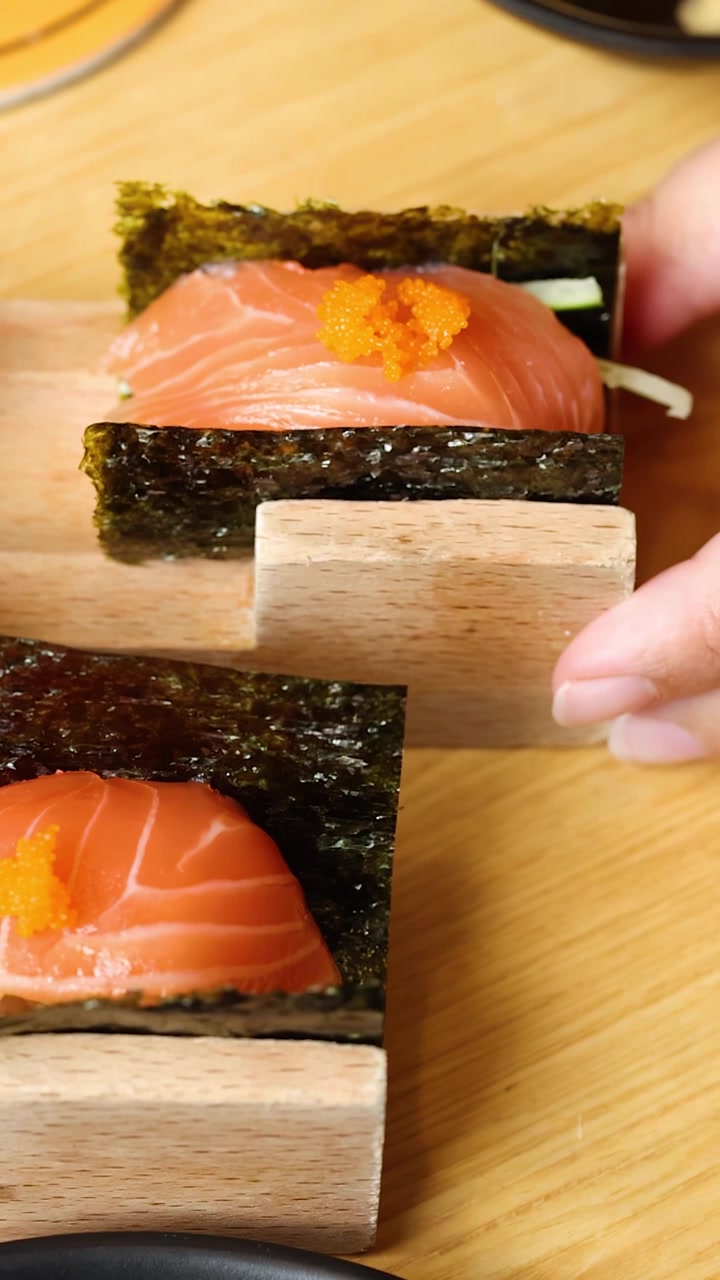 Primo piano di un hand roll di sushi al salmone disposto su un supporto di legno sotto una calda illuminazione da ristorante.
