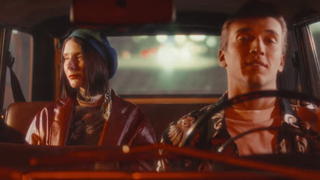 man driving vintage car at night with smiling woman sitting behind