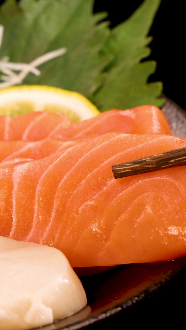 Primo piano di bacchette di legno che sollevano una fetta di sashimi di salmone fresco da un piatto.