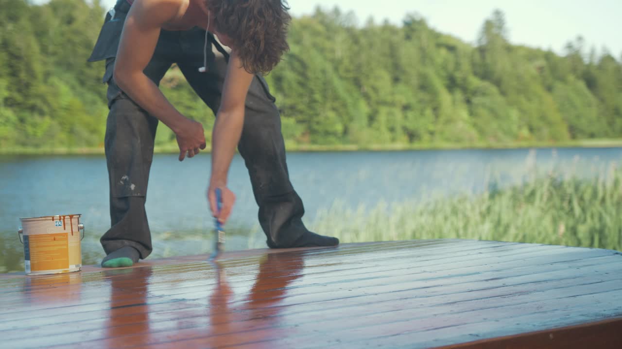 bondex 외부 보호 페인트로 나무 보트 선실의 지붕을 칠한 젊은 남자