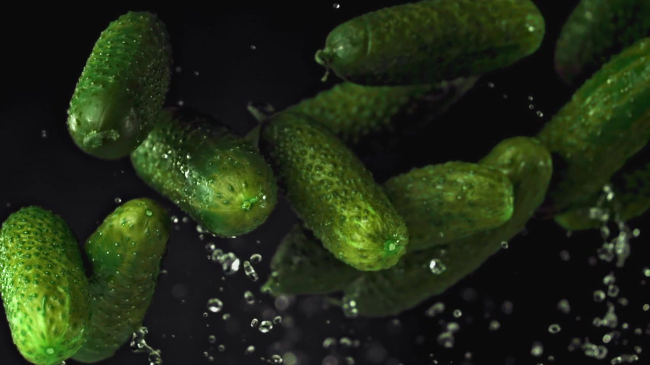 Cetrioli verdi freschi che cadono con schizzi d'acqua al rallentatore.