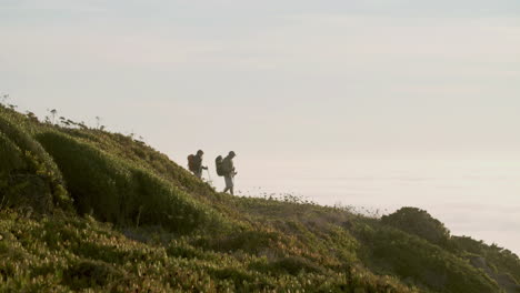 senior couple with backpack raising arms up while going down hill with trekking sticks