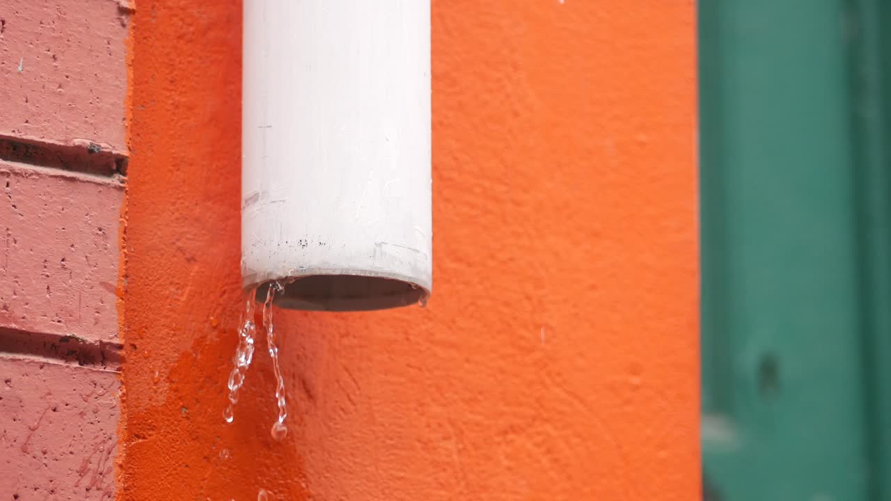 Water dripping from a white gutter on an orange wall