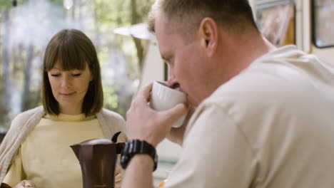 happy parents drinking coffee while having breakfast with their little sons at the camping in the forest