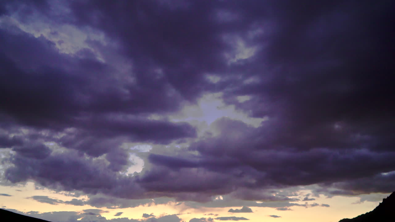 incline hacia abajo la toma amplia de una oscura puesta de sol en las montañas mientras la luz se refleja en la parte superior del agua mientras el río fluye en primer plano