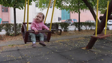 cute toddler swinging on wooden swing in city park