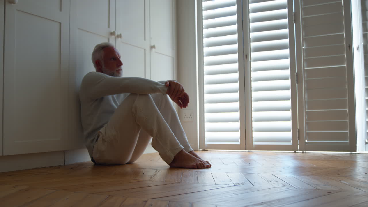 Depressed Senior Man Suffering With Poor Mental Health Sitting On Floor At Home