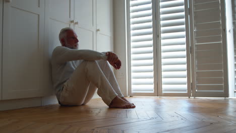 depressed senior man suffering with poor mental health sitting on floor at home