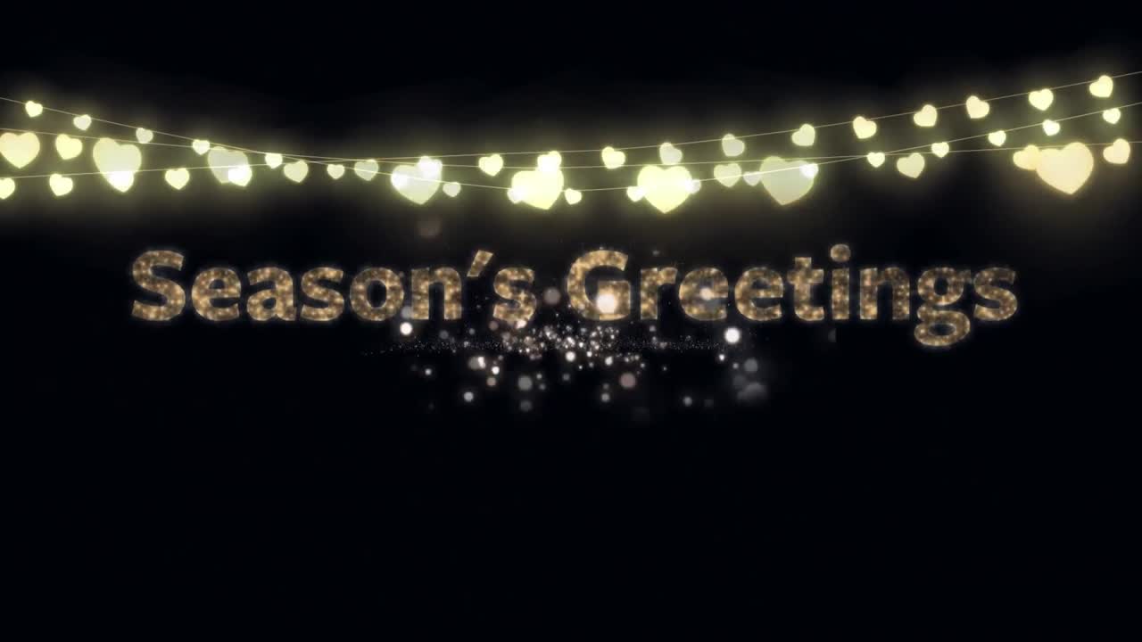 Animation of gold text season's greetings, with string of heart fairy lights and fireworks, on black