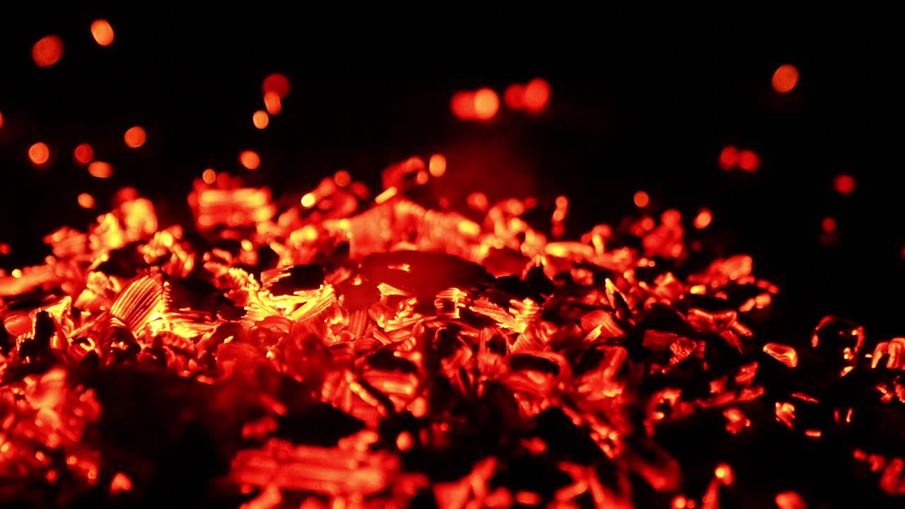 Hot smoldering parts of burnt wooden logs. Small sparkles fly to the sides. Close up. Black backdrop.