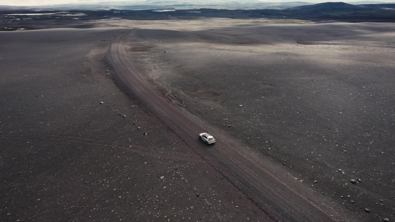 dron siguiendo un auto plateado filmado desde la izquierda conduciendo fuera de la carretera en el campo lunar de islandia en 4k